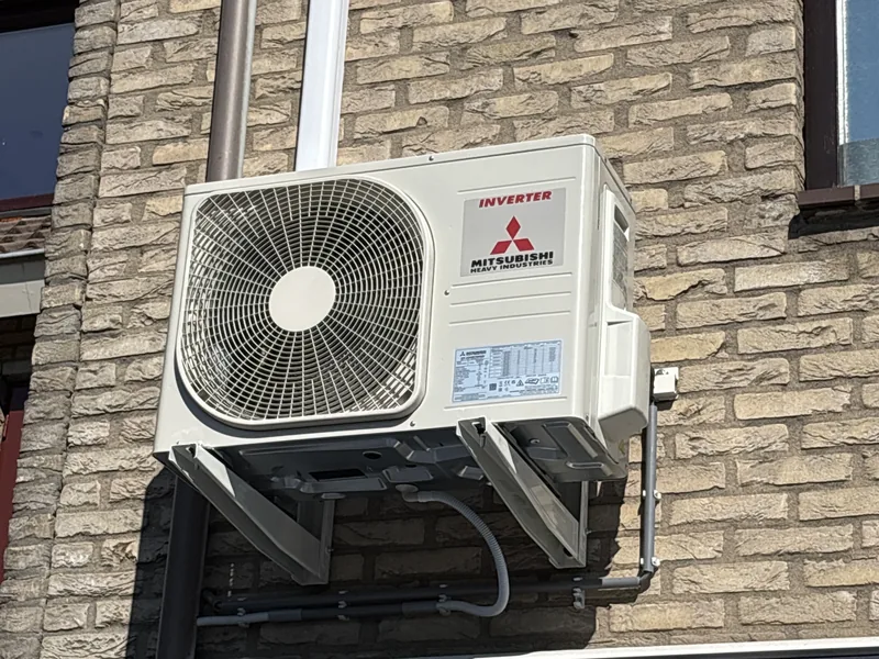 Buitenunit van een airco op een muurbeugel aan een bakstenen gevel