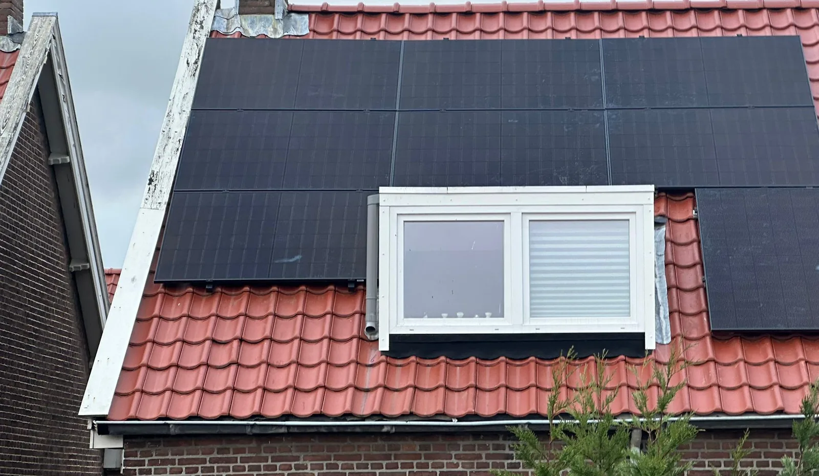 Rood pannendak met zwarte zonnepanelen rond een dakkapel