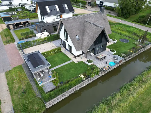 Woning met een rieten dak aan het water, met zonnepanelen op het bijgebouw