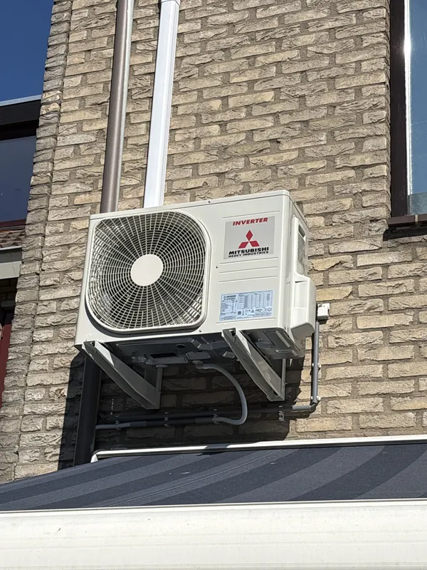 Buitenunit van een airco op een muurbeugel aan een bakstenen gevel