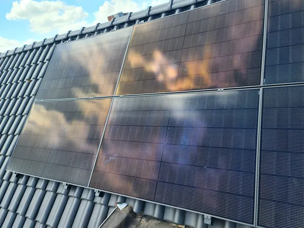 Zonnepanelen op een pannendak met weerspiegelende wolken