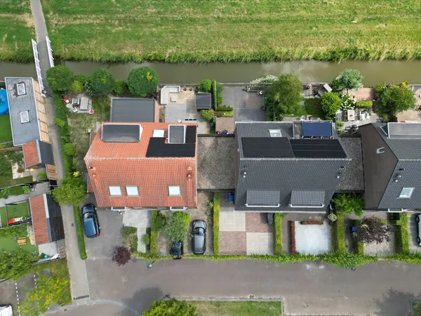 Twee woningen aan een sloot met zonnepanelen op de daken, van bovenaf