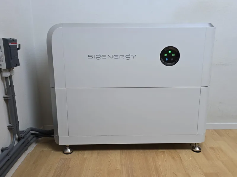 Witte Sigenergy-thuisbatterij op een houten vloer tegen een lichte muur