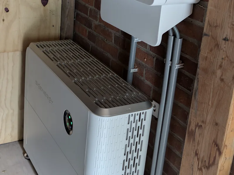 Hybride omvormer aan de wand met een thuisbatterij eronder, in een houten kast