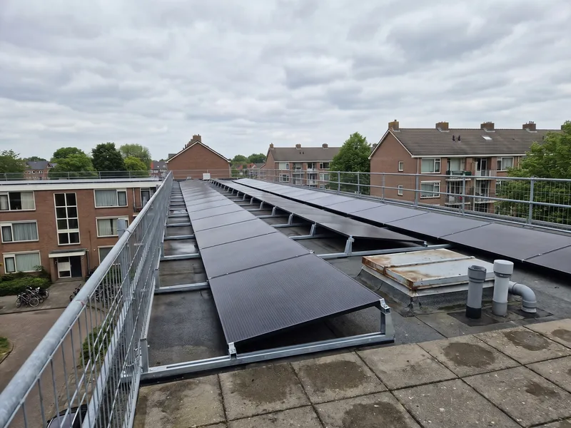 Lange rijen zonnepanelen op het dak van een appartementencomplex, met een veiligheidshek