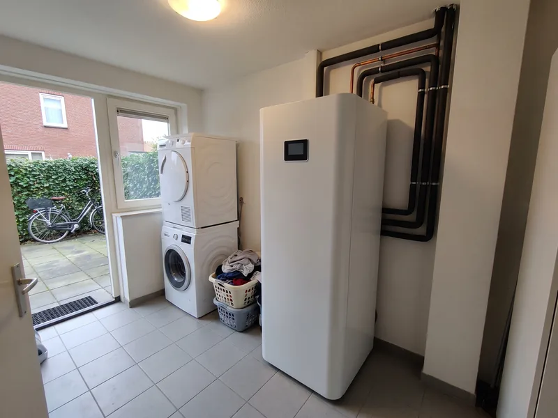 Witte binnenunit met boilervat in een bijkeuken naast de wasmachine