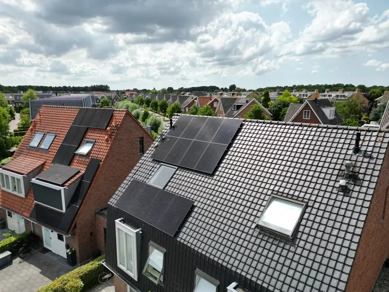 Donker pannendak met zwarte zonnepanelen en dakramen in een woonwijk
