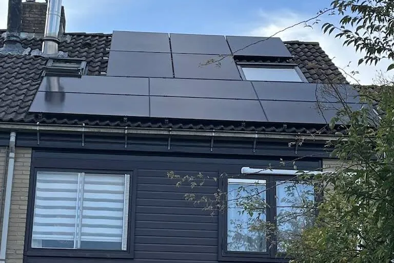 Zwarte zonnepanelen op een dak boven een donkere gevel